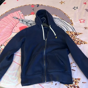 Blå huvtröja från Ralph Lauren  - Säljer en mörkblå polo Ralph lauren hoodie som är väldigt fräsch nu till vintern och våren den sitter riktigt bra samt som den är lätt att matcha. Tröjan är i väldigt bra skick har använts ett fåtal gånger. Nypris på denna tröja var 1.800kr.