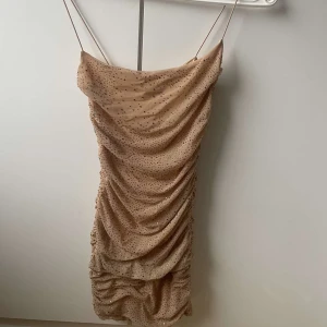 Champagnefärgad klänning med paljetter - Säljer en elegant champagnefärgad klänning med tunna axelband och glittriga paljetter. Klänningen har en draperad design och en dragkedja bak. Perfekt för en festlig kväll! Den är från oh polly, skriv för mer bilder eller frågor