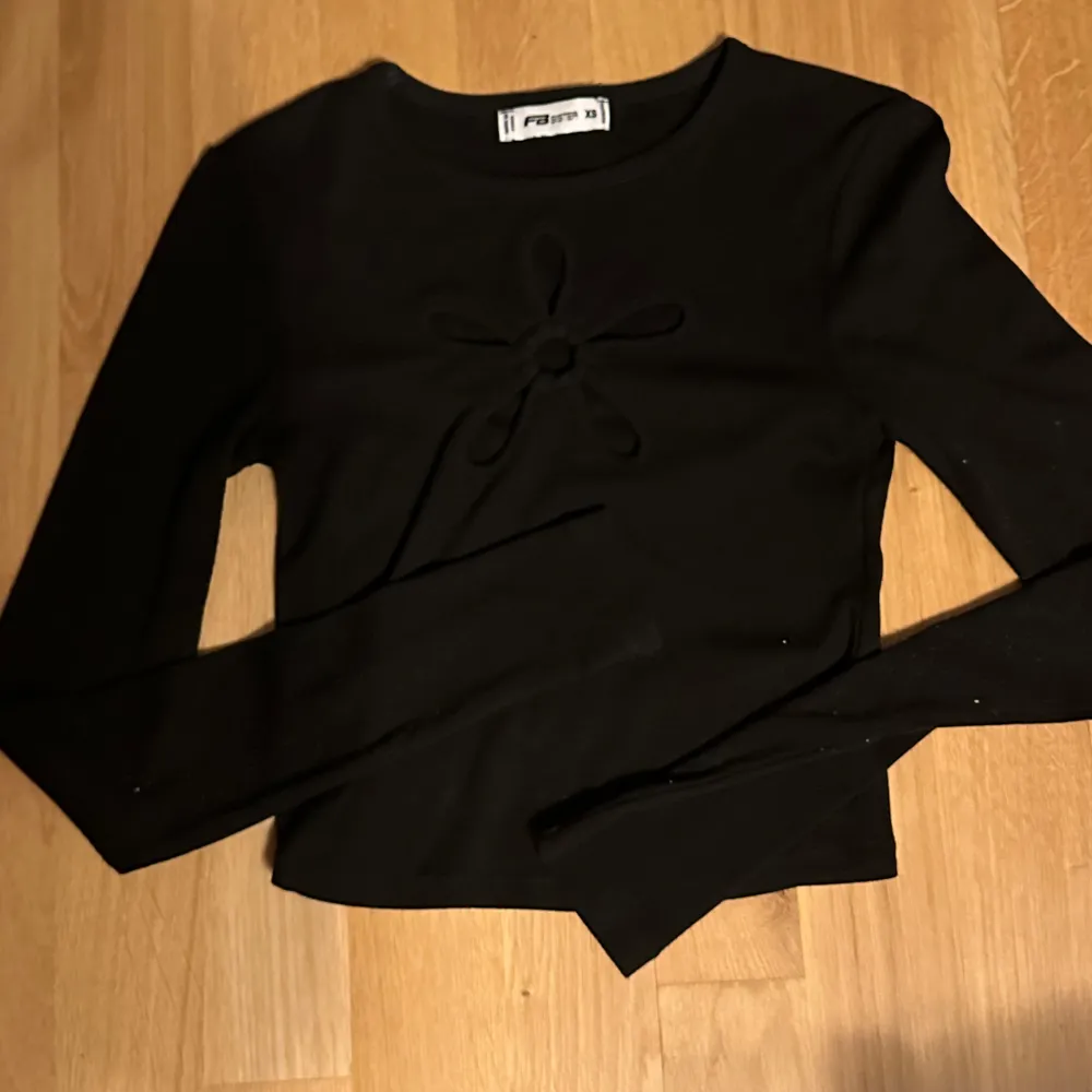 Snygg svart långärmad topp från FB Sister i storlek XS. Toppen har en unik blomdetalj framtill som visar vad som finns undertill. Perfekt för att styla med dina favoritjeans eller kjol. använd två gånger. Neuletakit & Villapaidat.
