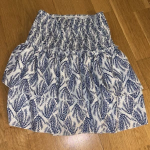 Blåvit kjol med bladmönster - Charmig blåvit kjol med ett vackert bladmönster. Kjolen har en elastisk midja och volangdetaljer som ger en luftig känsla. Jag skulle säga att den går att andvönda i många olika storlekar då den är jätte uttöjbar💞skriv om du vill ha fler bilder💞