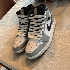 Nike Air Jordans i grått och vitt - Snygga Nike Air Jordans i grått och vitt med svart swoosh. Skorna har hög modell med snörning och perforerad tå för extra ventilation. Perfekta för en stilren look. Jag köpte dom och sedan har aldrig använt dom säljer dom för 1200 men nytt pris är 2999