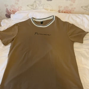 Beige t-shirt med texten 'Femme' med short - Säljer en beige t-shirt med texten 'Femme' tryckt på bröstet. T-shirten har en rund halsringning med vit och svart kant och korta ärmar. Perfekt för en avslappnad stil.