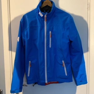 Blå vindjacka från Helly Hansen - Säljer en blå vindjacka från Helly Hansen med vit dragkedja och logotypdetaljer på bröstet och ryggen. Den är 8/10 riktigt fett. Om du har någon fråga är det bara att skriva! 💙
