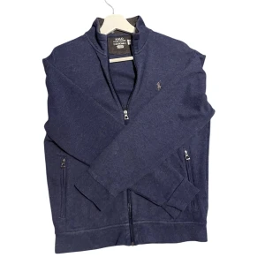 Mörkblå tröja från Polo Ralph Lauren - Säljer en stilren mörkblå tröja från Polo Ralph Lauren. Tröjan har en dragkedja framtill och två fickor med dragkedjor. Den är helt ny! En bit av prislappen sitter kvar. VÄLJ POSTNORD!