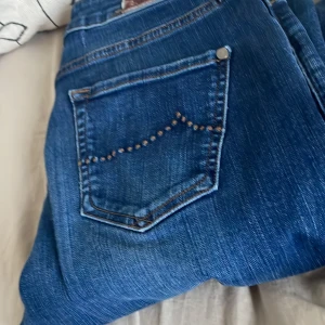 Blå jeans - Snygga blå jeans med dekorativa nitar på bakfickan. Perfekt för en cool och avslappnad stil. Klassisk femficksdesign och knappgylf.