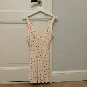 Vit klänning med jordgubbsmönster från Zara - Söt vit klänning från Zara med ett superfint jordgubbsmönster. Klänningen har en v-ringad design och är ärmlös, perfekt för varma sommardagar. Den korta längden ger en avslappnad och trendig look. 🍓