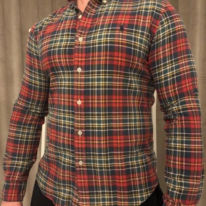 Rutig skjorta från Ralph Lauren - Snygg rutig skjorta från Ralph Lauren i rött, blått och gult. Skjortan har en slim fit passform och är långärmad med knappar framtill. Perfekt för en stilren look.