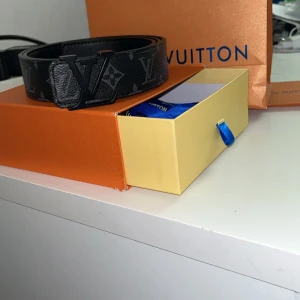 Svart bälte från Louis Vuitton(med kvitto och original förpackning) - Säljer ett stilrent svart bälte från Louis Vuitton med det ikoniska monogrammönstret. Bältet har en elegant svart spänne med LV-logotypen. Perfekt för att ge en lyxig touch till din outfit.