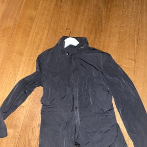 Svart vindjacka med dragkedja - Snygg svart vindjacka med dragkedja och hög krage. Jackan har långa ärmar och flera praktiska fickor framtill. Perfekt för blåsiga dagar och ger en cool look. 🖤