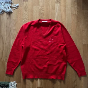 Röd PGA 1984 golf  ulltröja från Dunbrae - Säljer en klassisk röd tröja från Dunbrae i 100% lammull. Tröjan har en v-ringad hals och broderad text 'PGA Penina 1984' på bröstet. Perfekt för kyliga dagar med sin mjuka och varma ullkvalitet. Tillverkad i Skottland.