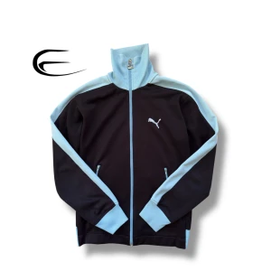 Svart och ljusblå tröja från Puma - Snygg svart och ljusblå tröja med dragkedja från Puma med dragkedja och hög krage. Perfekt för en sportig look. Jackan har långa ärmar och en stilren design med Puma-loggan på bröstet.