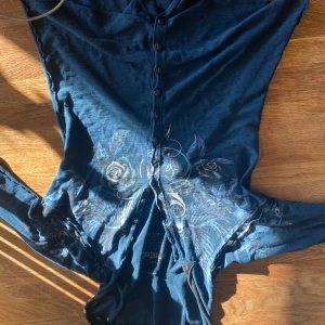 Alt Blå hoodie från Sinful av affliction - Snygg blå hoodie från Sinful med knappar framtill och ett coolt tryck av rosor och fåglar. As skön. Den har långa ärmar och en bekväm passform. Bra skick 