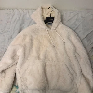 Vit teddyjacka med huva - Mysig vit teddyjacka från Discovery Expedition med huva och känguruficka. Perfekt för kyliga dagar när du vill hålla dig varm och bekväm. Jackan har en fluffig textur och ribbade muddar vid ärmslut och nederkant.