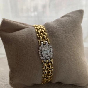 Guldplatärat med glittrig detalj - Elegant guldplatärat armband med en glittrig rektangulär detalj i mitten. Armbandet har en länkdesign som ger en lyxig känsla. Perfekt för att lägga till en touch av glamour till din stil.