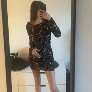 Svart glittrig klänning från Nelly med öppen v-ringad rygg - Snygg svart klänning från Nelly med glittriga paljetter och långärmad design. V-ringad rygg (se bild 2). Aldrig använd så i helt nyskick. Normal i storleken