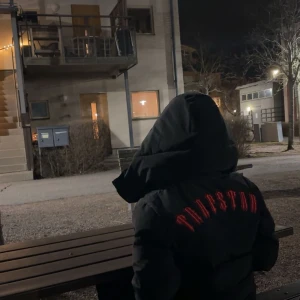 Trapstar jacka - Säljer en svart pufferjacka från Trapstar med röd text på ryggen. Jackan har en stor huva och är perfekt för kyliga dagar. Den är både stilren och funktionell, vilket gör den till ett måste i garderoben. Passar bra för vinterns kalla väder. S men passar även M