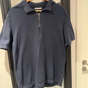 Mörkblå pikétröja från Zara - Säljer en stilren mörkblå pikétröja från Zara med dragkedja framtill. Tröjan har korta ärmar och en klassisk krage, perfekt för en avslappnad look.