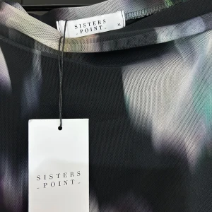 Mönstrad kjol från Sisters Point - Snygg skjol från Sisters Point med ett abstrakt mönster i olika färger. Klänningen har en draperad design och är perfekt för en unik look. Den är tillverkad i ett mjukt och bekvämt material.