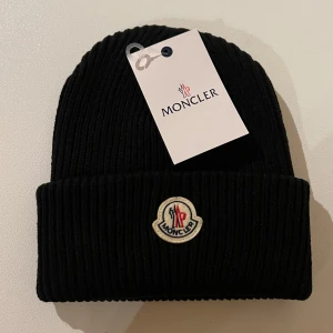 Moncler Mössa - Snygg svart ribbad mössa från Moncler med broderad logotyp framtill. Perfekt för att hålla värmen under kyliga dagar.