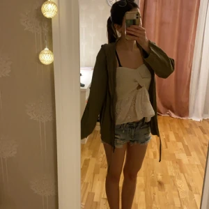 Olivgrön linne jacka med huva - Säljer en olivgrön linne blandad jacka med huva och dragkedja framtill. Jackan har långa ärmar och en justerbar dragsko i nederkanten. Perfekt för en avslappnad stil.