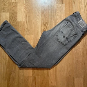 Grå jeans från Replay - Snygga grå jeans från Replay med klassisk femficksdesign och diskret broderad detalj på bakfickan. Perfekta för en stilren look. Märkeslogga synlig vid fickan.