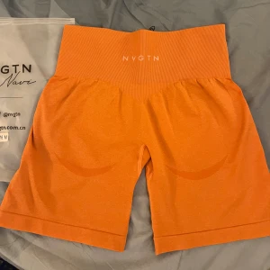 Orange shorts från NVGTN - Snygga orange shorts från NVGTN med hög midja och ribbad detalj upptill. Perfekta för träning med en bekväm passform. Materialet är stretchigt och andas bra, vilket gör dem idealiska för aktiva dagar.