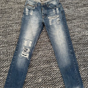 Adrian hammond slitna jeans - Snygga blå jeans med slitningar och broderad detalj på bakfickan. Perfekta för en avslappnad stil.