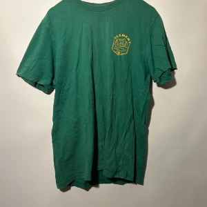 Element t-shirt - Grön t-shirt med tryck på både fram- och baksidan. Trycket har motiv av berg och texten 'Element'. Urtvättad men annars bra skick.