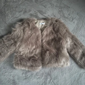Beige pälsjacka från Wynn - Säljer en snygg beige pälsjacka från Wynn. Jackan har en fluffig och lyxig känsla med långa ärmar och en öppen front. Perfekt för att ge din outfit en extra touch av glamour.