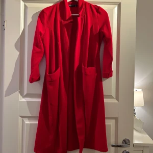 Röd kappa - Snygg röd kappa med långa ärmar och öppen design. Perfekt för att ge en färgklick till din outfit. Den har praktiska fickor framtill och en stilren look.