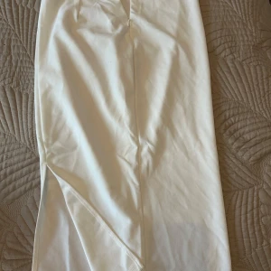 Vit långkjol - Elegant vit långkjol med en stilren design. Kjolen har en slits som ger extra rörelsefrihet och en modern touch. Perfekt för att skapa en chic look.