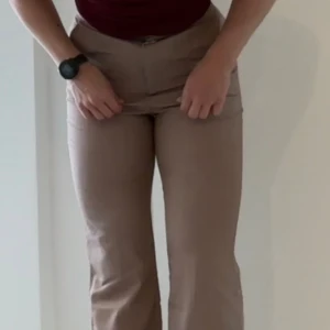 Beige byxor med hög midja - Säljer ett par snygga beige byxor med hög midja. De har en rak passform och är perfekta för både vardag och fest. Byxorna har en dragkedja framtill och är gjorda i ett bekvämt material som ger en stilren look.