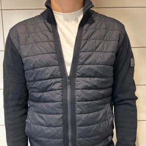 Mörkblå quiltad jacka - Säljer en snygg mörkblå jacka med quiltad framsida och stickade ärmar. Jackan har en dragkedja framtill och en hög krage som håller dig varm. Perfekt för höst och vår!           skick 9/10