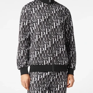 Svartvit bomberjacka från Phillip Plein - Säljer en snygg svartvit bomberjacka från phillip Plein med ett coolt all-over print av märkesnamnet. Jackan har en dragkedja framtill och ribbade muddar vid ärmslut och nederkant. Perfekt för att sticka ut på festen eller bara chilla i vardagen.