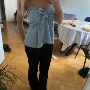 Ljusblå axelbandslös topp - Säljer en superfin ljusblå axelbandslös topp med en stor rosett framtill. 