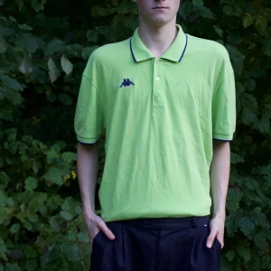 Grön pikétröja från Kappa - Säljer en grön pikétröja från Kappa i storlek M. Tröjan har korta ärmar och en klassisk krage med mörkblå detaljer. Perfekt för sommardagar eller en avslappnad stil. Skön och luftig, idealisk för både vardag och fritid.
