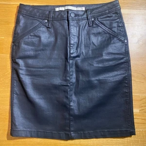 Svart jeanskjol i lite vaxat material i strl 34 från Part Two - Svart jeanskjol i lite vaxat material i strl 34 från Part Two.  Sparsamt använd och i fint begagnat skick.  Mått Midjan: ca 38 cm Total längd: ca 50 cm  98% bomull och 2% elastan  Kommer från ett djur och rökfritt hem.