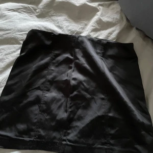 Svart mini / kort kjol från Gina Tricot  - Säljer en svart minikjol från Gina Tricot i storlek xs. Den har en liten dragkedja i midjan och har satinliknande material. Inte så stretchig i midjan 