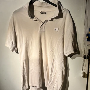 Vit pikétröja från Acne Studios - Säljer en stilren vit pikétröja från Acne Studios i bra skick. Tröjan har en klassisk krage och korta ärmar, perfekt för både vardag och fest. Den är gjord i mjukt bomullsmaterial och har en diskret broderad logga på bröstet. Passar perfekt för vår och sommar! Köpt för 2000 hos Acne Studios i Stockholm. Tveka inte att höra av dig om du har frågor eller vill ha fler bilder!