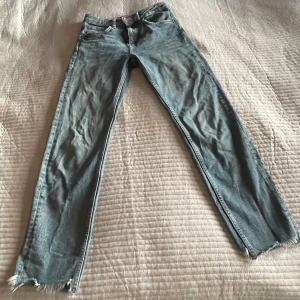 Blå jeans från Zara - Säljer ett par snygga blå jeans från Zara i storlek 24. De har en fransig kant vid bensluten och är tillverkade av ekologisk bomull. Perfekta för en avslappnad stil och passar bra till både vardag och fest. Använda men i bra skick!