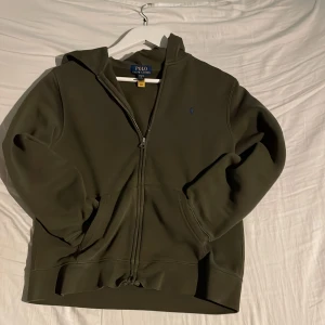 Grön ziphood från Ralph Lauren - Säljer en snygg grön ziphood från Ralph Lauren i storlek XS. Tröjan är unik med en blå häst. Perfekt för höst och vår när du vill hålla det casual men stilrent. Skicket är mycket bra, inga defekter!😄