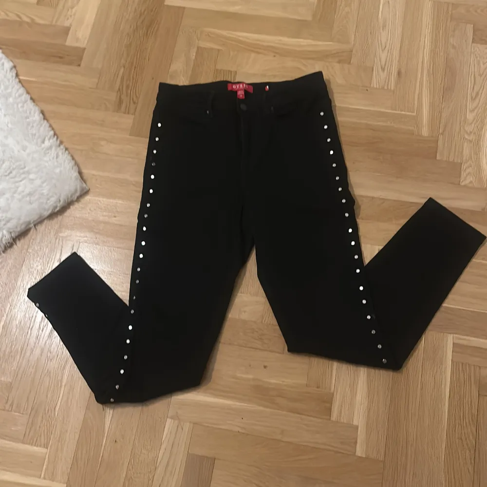 Snygga svarta jeans från Guess med coola nitar längs sidorna. De är högmidjade och har en slim passform som sitter perfekt. Perfekta för en utekväll eller när du vill känna dig extra stylish. De är i mycket bra skick och redo för nya äventyr!. Farkut & Housut.