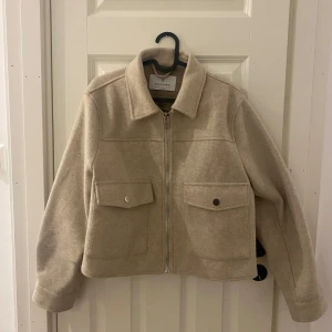 Beige jacka från Stradivarius - Säljer en snygg beige jacka från Stradivarius i mycket bra skick. Jackan har en dragkedja framtill och två stora fickor med knappar. Perfekt för höst och vår, och den har en normal passform. Superfin att matcha med jeans eller kjol!