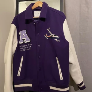Axel Arigato ”Varsity Jacket” Storlek S - Säljer en snygg lila och vit Superfin limited edition Axel Arigato Varsity bomber i storlek S och färgen lila som inte säljs längre. Passar även M. Jackan är använd ett fåtal gånger (max 5 gånger). Nypris 4000kr.Jackan har broderade detaljer med text och ett flygplansmotiv. Den har knappar framtill och ribbstickade muddar. 