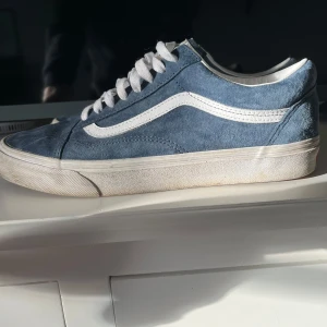 Blå sneakers från Vans - Säljer ett par klassiska blå Vans sneakers i mocka med vit sula och snörning.  Är i bra skick med lite slitage på sulan. Perfekta för vardagsbruk och ger en skön, avslappnad stil. Passar bra till både jeans och shorts!