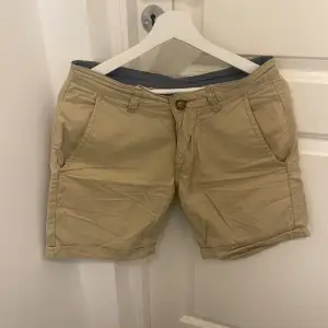 Säljer ett par snygga beige shorts från Lager 157 i storlek M. De är gjorda av 100% bomull och har en klassisk design med knappar och bälteshällor. Perfekta för sommardagar eller en avslappnad vårlook. Shortsens stilrena design gör dem lätta att matcha med olika outfits.