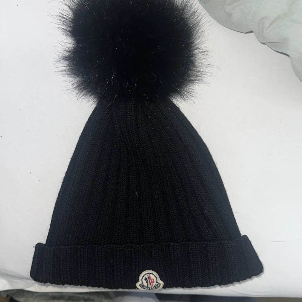 Snygg svart stickad mössa från Moncler med en stor fluffig pälsboll på toppen. Den har en uppvikt kant och Monclers logga framtill. Perfekt för att  hålla sig varm och stilren under vintern. Nypris 3250 kr jag säljer den för 1000 kr. Pris går och diskutera . Accessoarer.