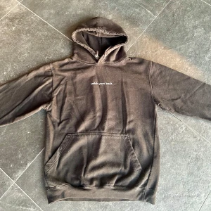 Svart hoodie med kattmotiv - Säljer en svart hoodie med texten 'watch your back' på framsidan och ett coolt kattmotiv i grönt och blått på baksidan. Perfekt för en avslappnad stil och passar bra till både höst och vår. Den har en stor ficka fram och är i bra skick.