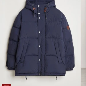 Gant Mörkblå pufferjacka  - Helt ny! Köpte fel storlek. Köpt för 4200kr på rea. Säljer en snygg mörkblå pufferjacka i mycket bra skick. Jackan har en dragkedja och knappar framtill, samt en praktisk huva. Perfekt för kalla vinterdagar och höstpromenader. Den är långärmad och har en normal passform. Superbekväm och stilren!