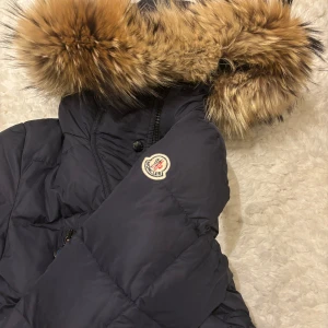 Marinblå dunjacka från Moncler - Säljer en snygg marinblå dunjacka från Moncler i mycket bra skick. Jackan har en fluffig pälsdetalj på huvan och är perfekt för kalla vinterdagar. Den har långa ärmar och stängs med både dragkedja och knappar. Supervarm och stilren! Köpt för flera år sedan för 8000. Säljer för 2500. Har en liten defekt på dragkedjan, se sista bilden❤️Strl 1, sitter som xs/s. 